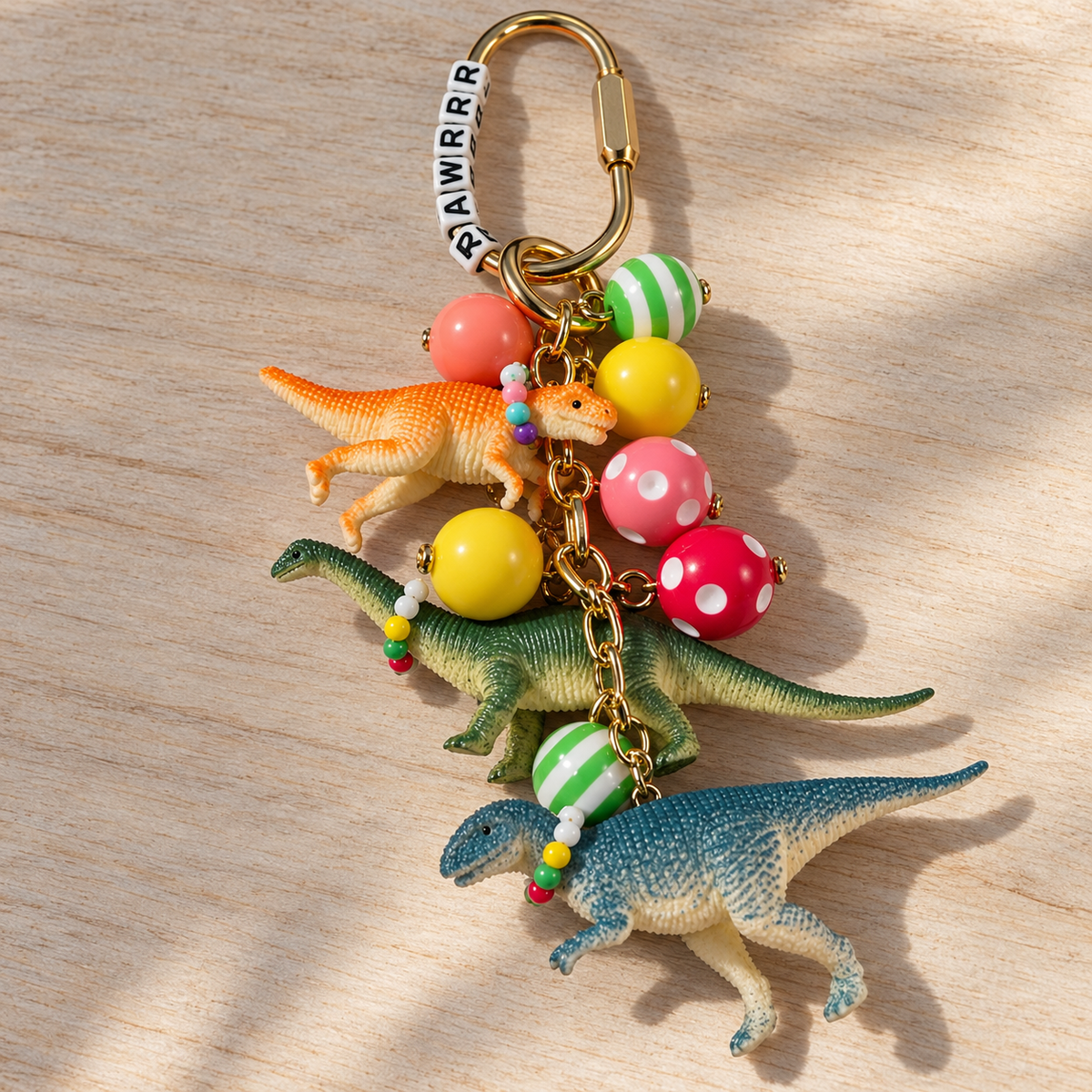 Dinosaur purse and backpack charm with three colorful dinosaurs wearing tiny necklaces, patterned resin beads, RRAWRRR letter beads, and a gold-tone clip.

